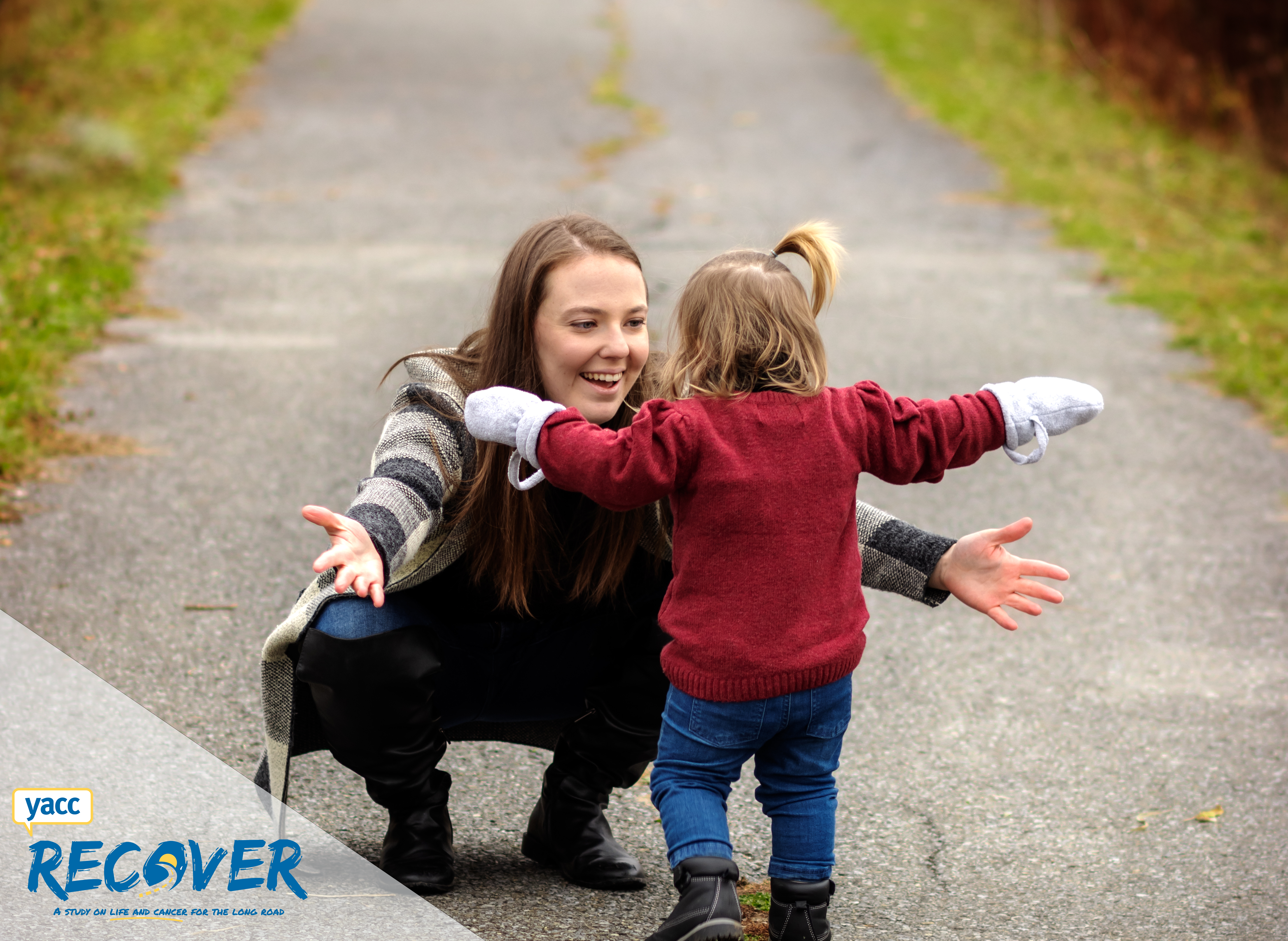 Gabrielle is crouched down with her arms outstretched toward her toddler. She has a large smile on her face. They are on a path outdoors. 
