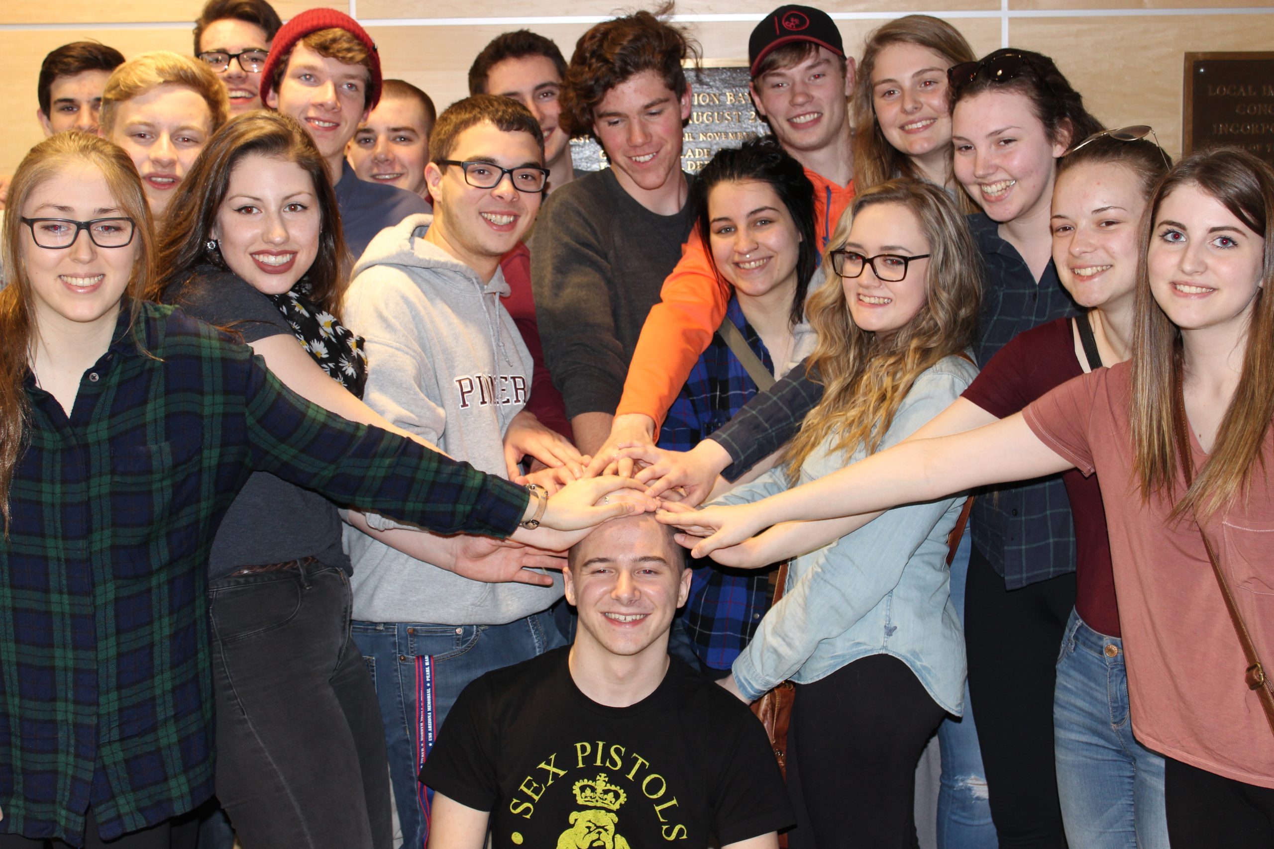 17 Student standing around Noah with their hands on his newly shaved head.