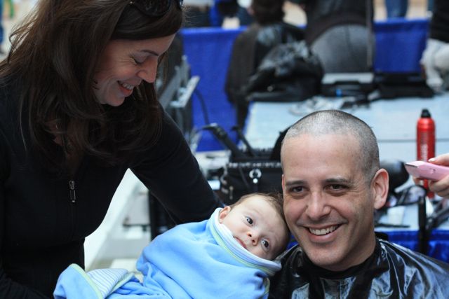 A man smiling with a baby and woman during his shave