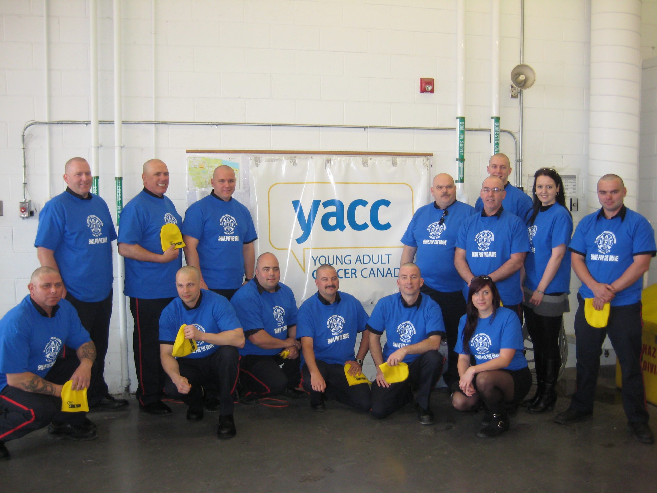 12 shavers and 2 mane mamas after their shave posing in front of a YACC banner