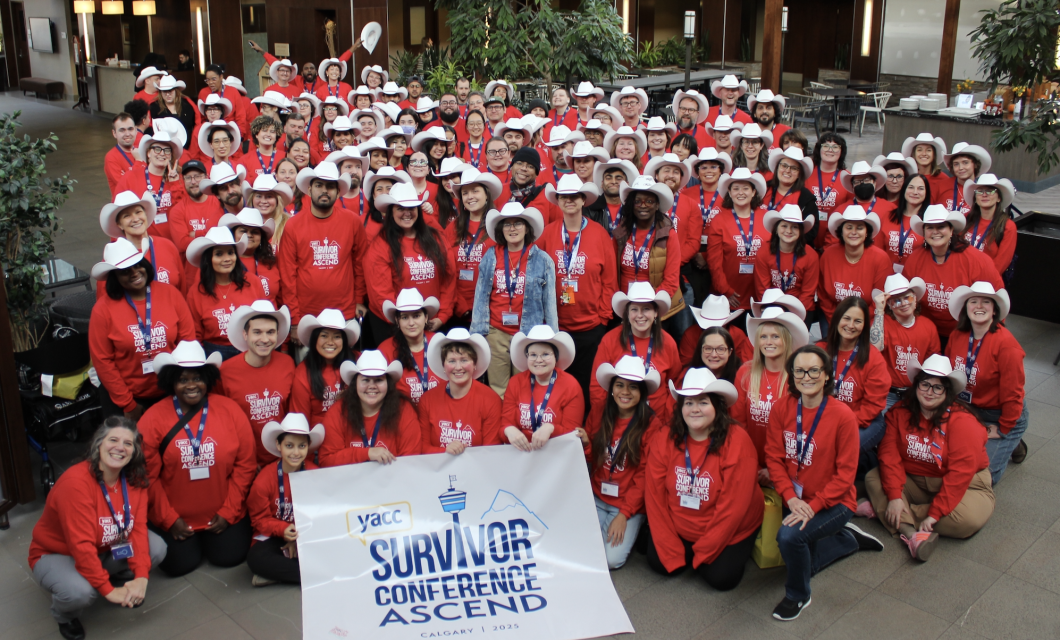 A group photo of over 100 young adults smiling at the camera in the hotel lobby. They are all wearing red shirts with a white conference logo on them, and most are wearing white cowboy hats from the Calgary Stampede.
