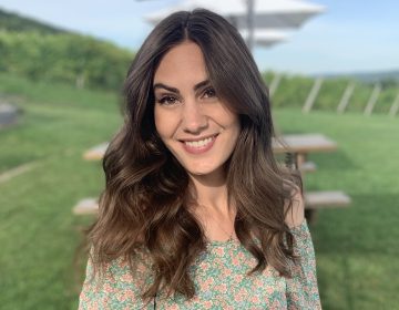 A medium shot of Ashley outside with a grassy background. She is wearing a light green dress, and her medium-length brown hair is in loose waves.